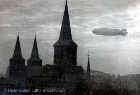 Die "Hindenburg" in Köln über dem Deutzer Hafen auf Fahrt nach Norden. Im Vordergrund St. Kunibert